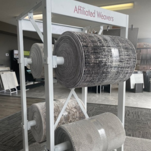 Display rack with various carpet rolls showcasing patterns and textures in a flooring showroom.
